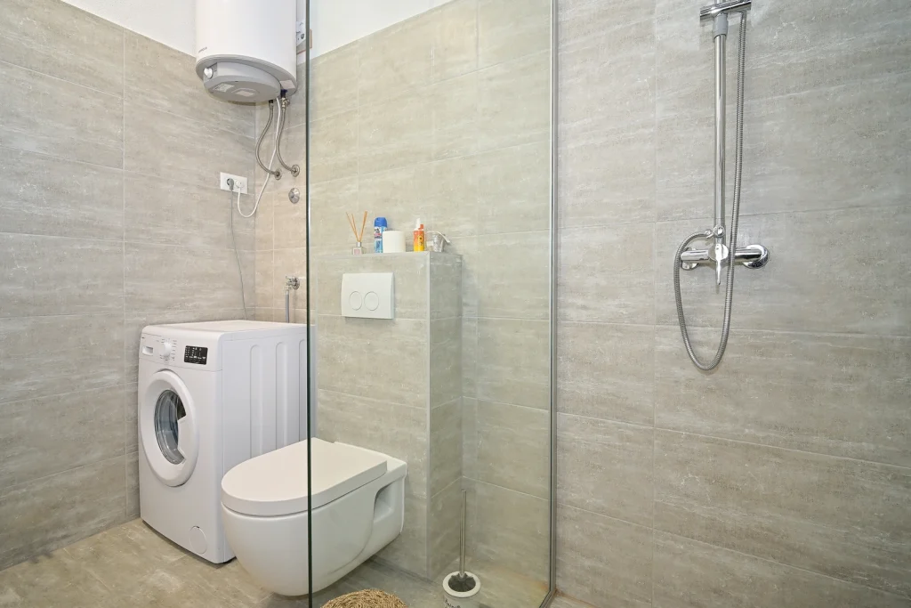 Kupaonica s perilicom rublja i tušem, širi kadar, apartman AMI Strožanac