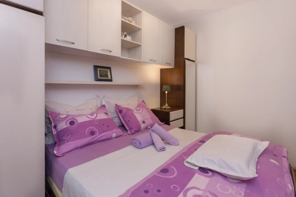 Udobna spavaća soba s bračnim krevetom i noćnim ormarićem u apartmanu Arca Strožanac